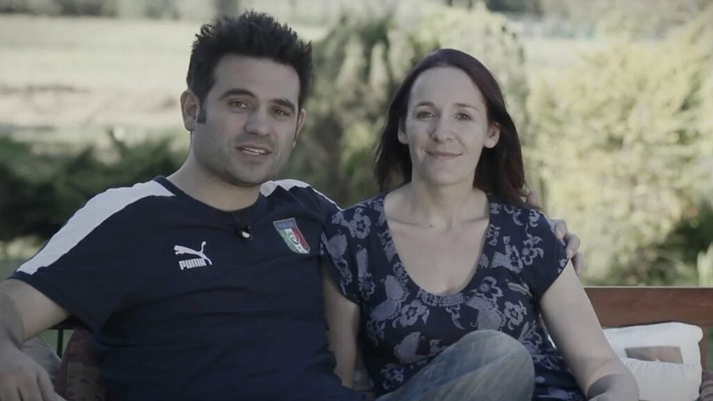 Euan and Karen MacRae seated outdoors on a bench, man with arm around woman, both looking at the camera