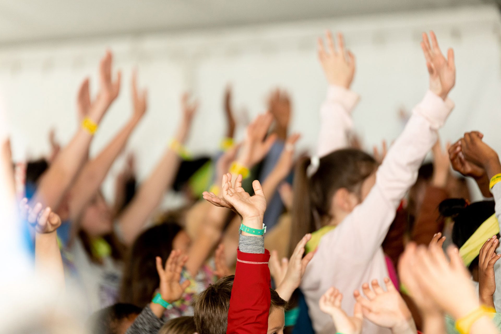 Group of children standing with hands raised during a church or youth activity, faces partly out of focus