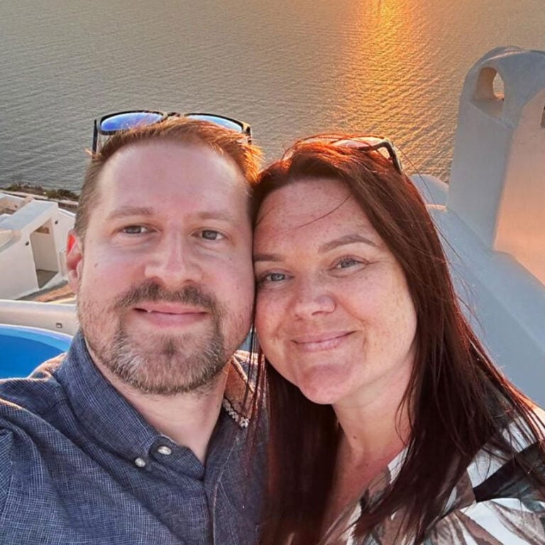 Alex and Sarah Blackford smiling in a close selfie with sea and sunset behind them