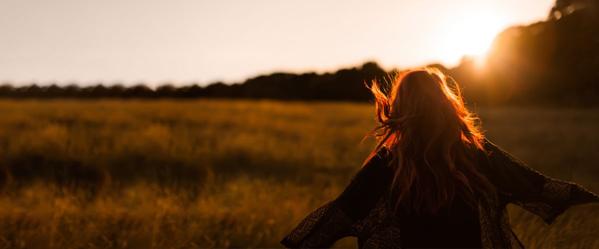 Rear view of a woman standing in a field at sunset with wind blowing her hair