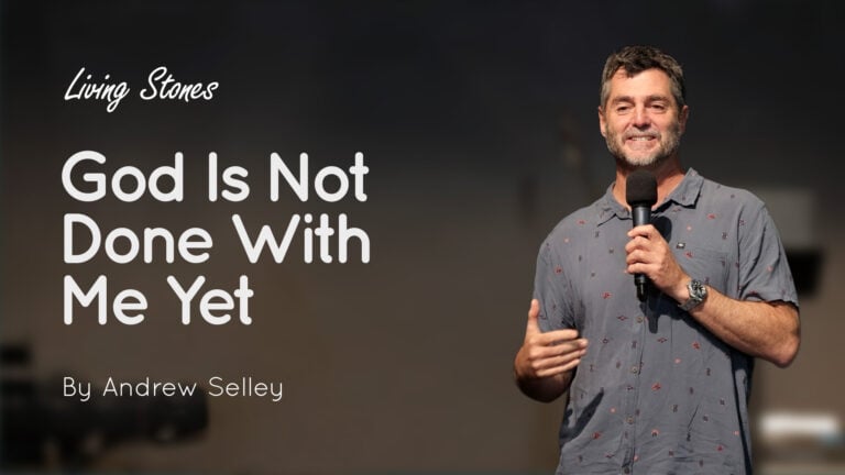 Speaker Andrew Selley on stage holding a microphone beside a slide titled ‘God Is Not Done With Me Yet’