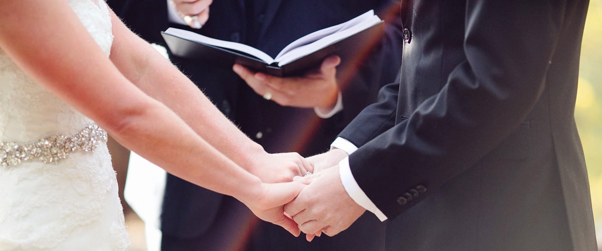 Bride and groom holding hands during a wedding ceremony while an officiant holds an open book