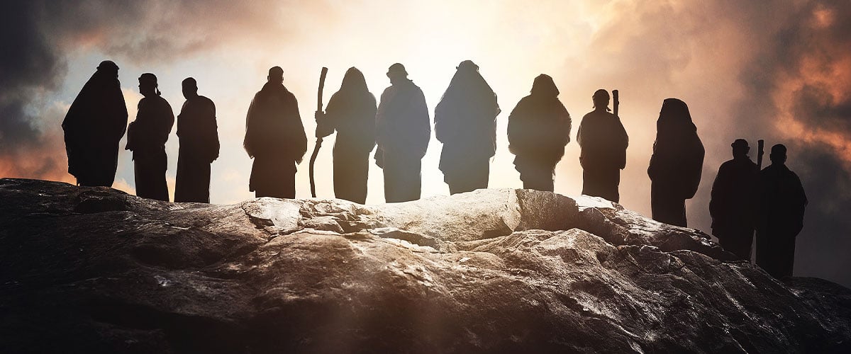 Silhouetted group of robed figures standing on a rocky ridge against a bright backlit sky