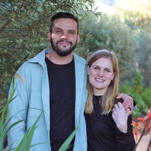 Johann & Cornelia van Deventer standing arm-in-arm outdoors, smiling with trees and plants in the background