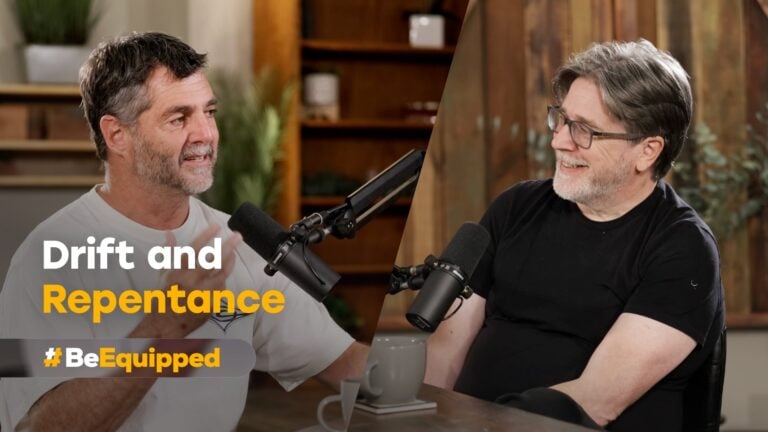 Two men seated at a table, speaking into microphones in a studio setting
