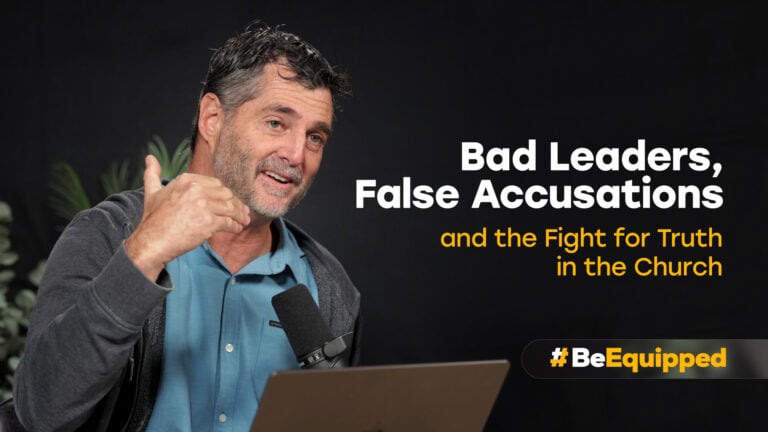 Middle-aged man speaking into a microphone and gesturing beside text reading 'Bad Leaders, False Accusations' on a dark