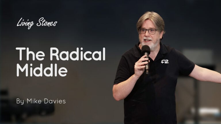 Man holding a microphone on stage beside a screen reading 'The Radical Middle'