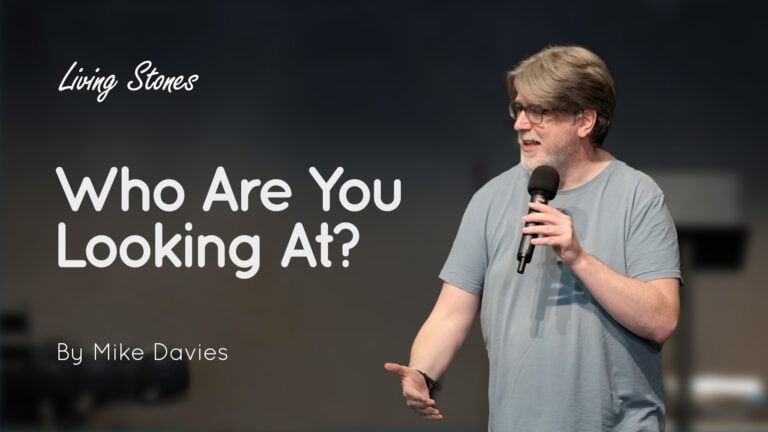 Man holding a microphone speaking on stage with the text 'Who Are You Looking At?' and 'By Mike Davies'