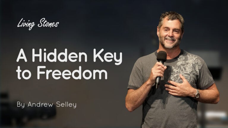 Andrew Selley speaking into a microphone beside title text 'A Hidden Key to Freedom' on a dark stage