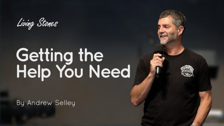 Man on stage holding a microphone with the words ‘Getting the Help You Need’ visible on a screen