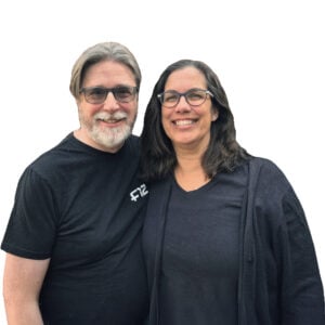 Smiling couple standing close together, both wearing glasses and dark tops