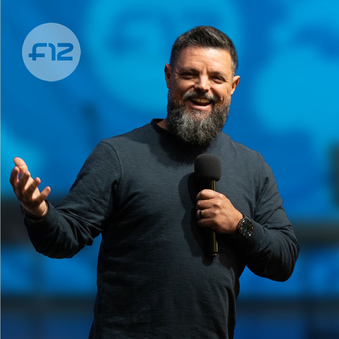 Bearded man holding a microphone and speaking on stage