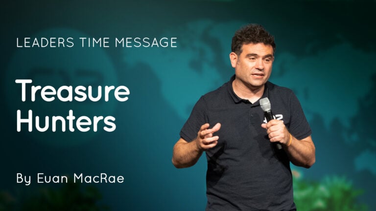 Male speaker on stage holding a microphone beside a teal slide titled ‘Treasure Hunters’