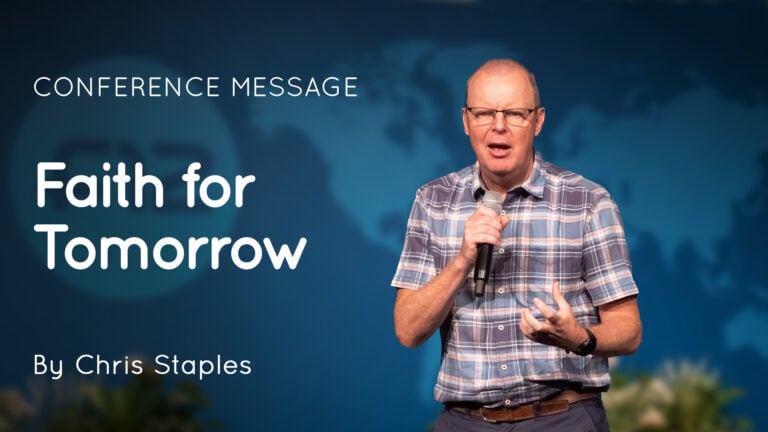 Chris Staples speaking into a handheld microphone on stage in front of a 'Faith for Tomorrow' conference backdrop