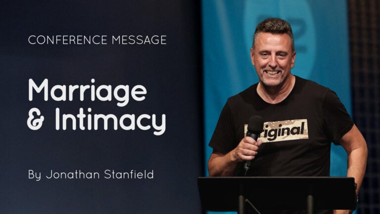 Speaker Jonathan Stanfield smiling at a lectern holding a microphone during a conference message titled “Marriage & Intimacy”
