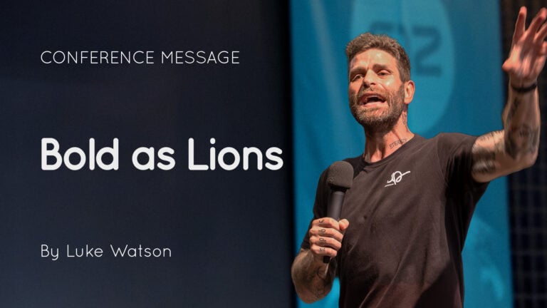 Speaker Luke Watson holding a microphone and gesturing on stage beside a slide reading ‘Bold as Lions’