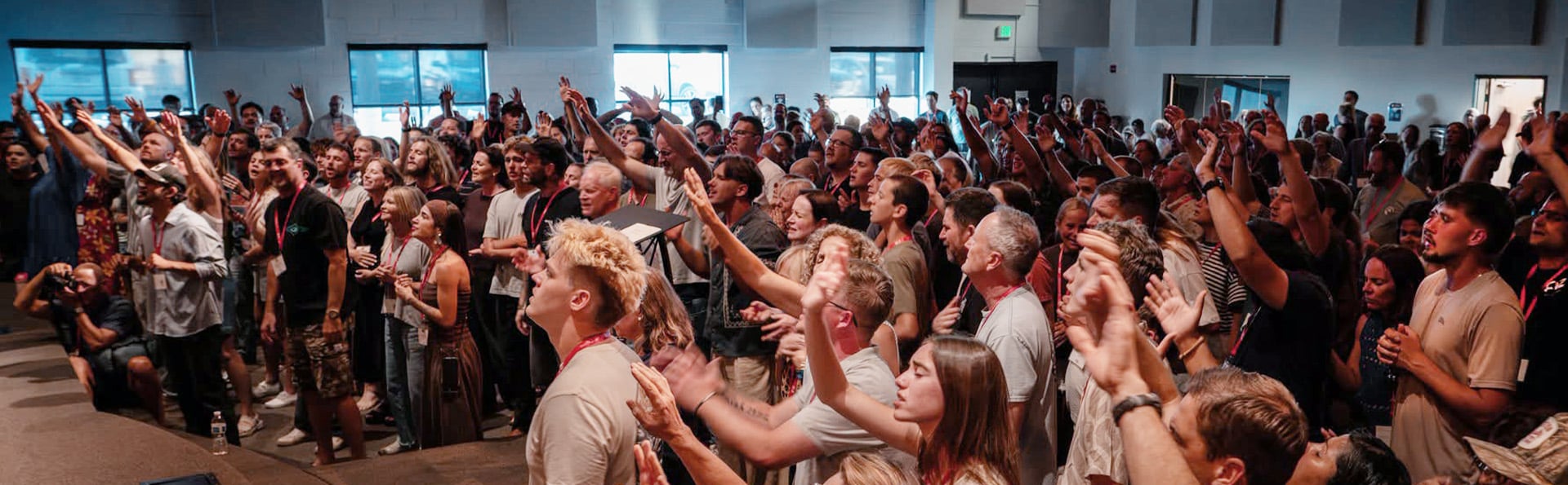 Large group of conference attendees standing indoors with many people raising hands