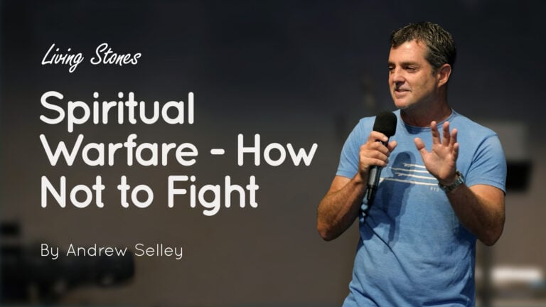 Andrew Selley holding a microphone and speaking beside a slide titled 'Spiritual Warfare - How Not to Fight'
