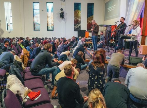 People kneeling and praying in a church auditorium as speakers and musicians lead from a stage at the 2024 School of