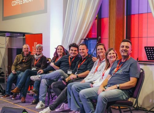 Eight leaders and speakers seated on stage smiling during the School of Leadership 2024 event