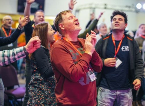 Group of conference participants with eyes closed and hands raised in a moment of worship or reflection
