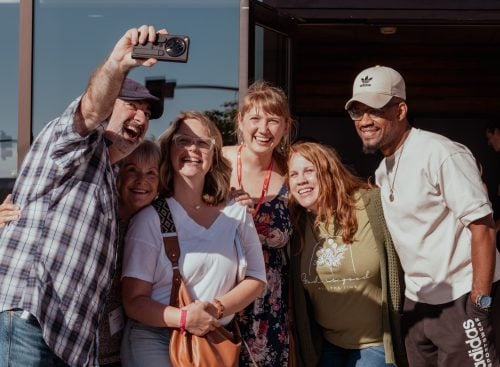 Six conference attendees smiling as a man takes a selfie outside a building at the 2025 conference in the USA