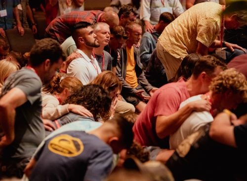 Group of people kneeling and praying at a conference, some laying hands on others