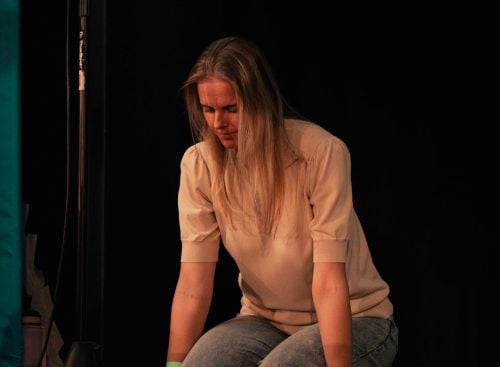 Person kneeling on stage with hands on the floor near a microphone stand
