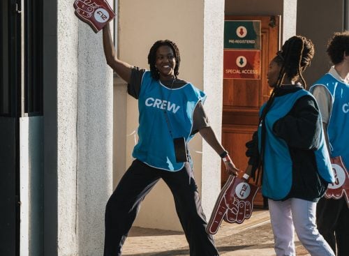 Event crew members in blue vests standing outside a building, holding foam finger signs