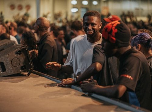 Young man smiling at the edge of a stage with others at a crowded indoor event