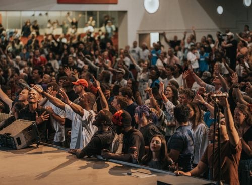 Large congregation standing near a stage, many people with raised hands in worship