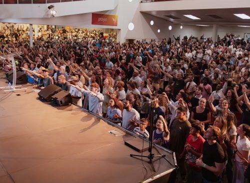 Crowd of conference attendees standing and raising hands toward the stage in a large church auditorium